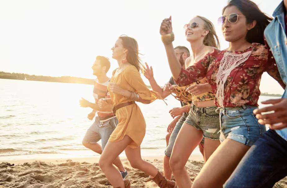 Group of young adults dancing and running on the sand at sunset, enjoying at beach festivals by the ocean.