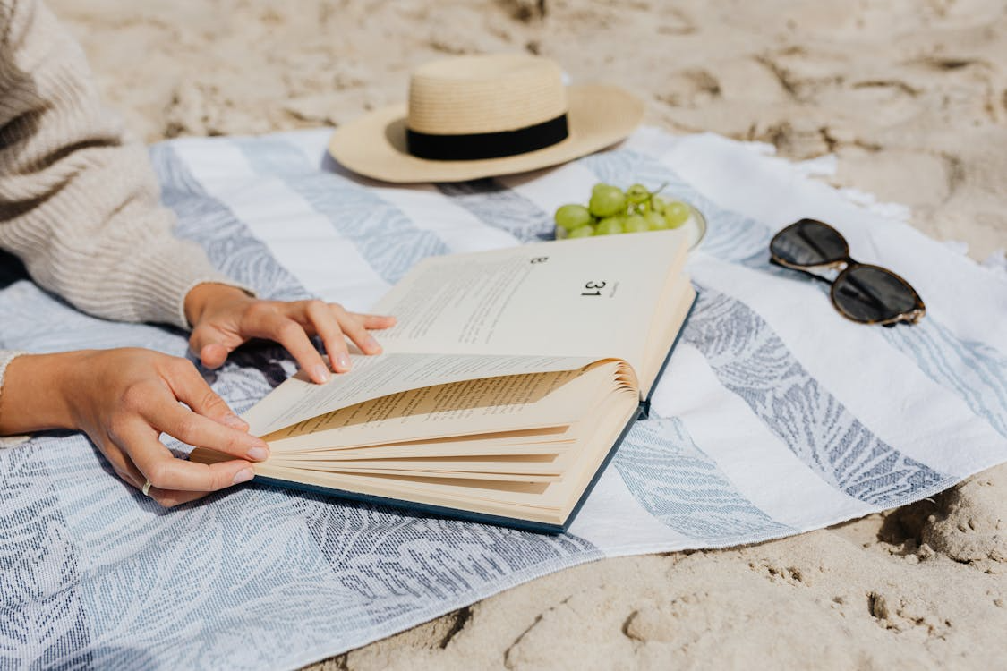 Person enjoying one of the best beach reads in 2025 while relaxing on the sand.
