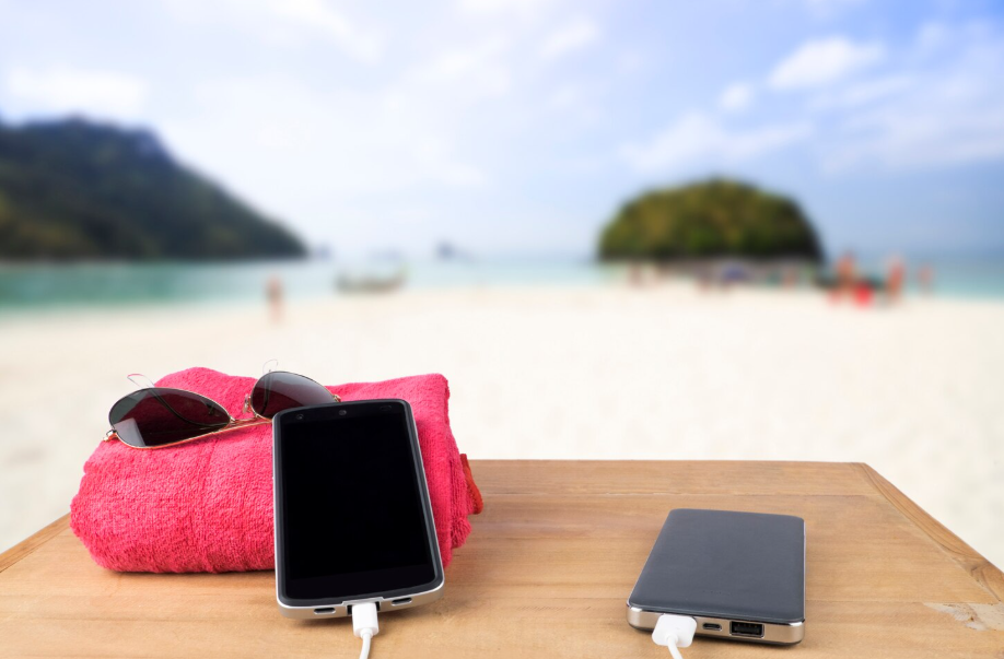 Smartphone charging with portable power bank on wooden table by the beach