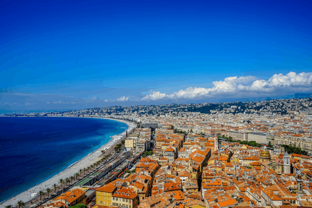 Aerial view of Nice, France, showing the Promenade des Anglais, turquoise coastline, and terracotta rooftops along the French Riviera.