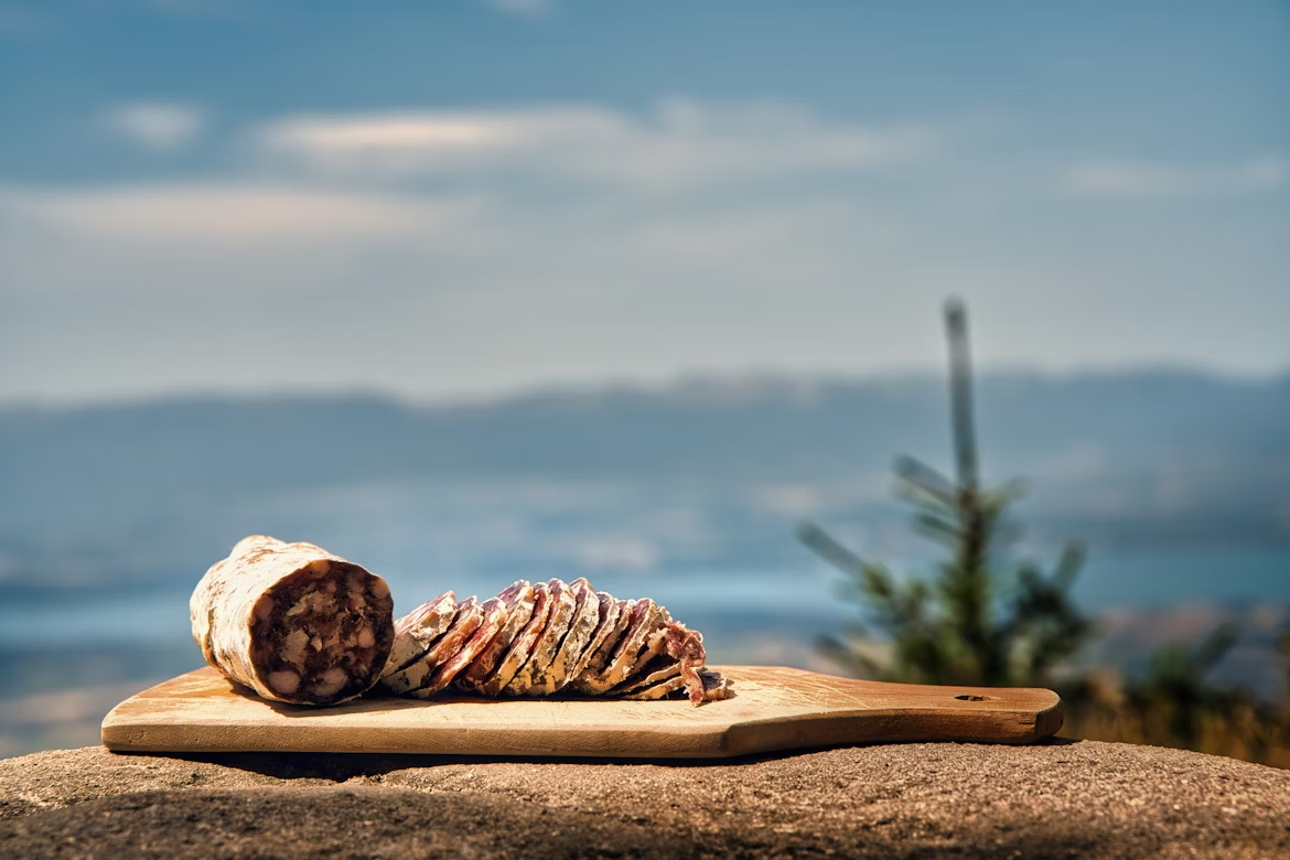 Sliced cured meat on a wooden board overlooking the sea during a coastal foodie road trip